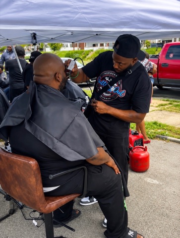 Barber trimming a client's hair under an outdoor canopy