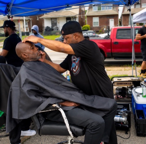 Barber working on a seated client's haircut outdoors