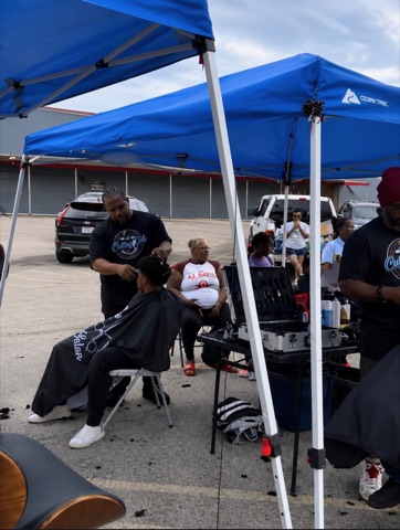 Barber cutting hair at a community event under blue tents